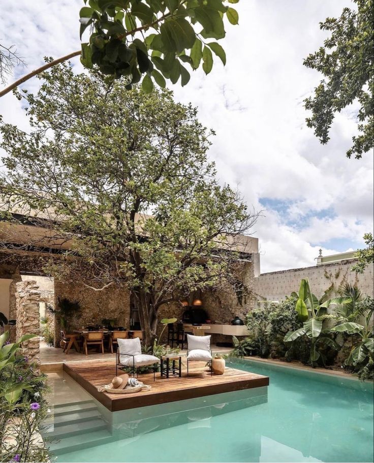 an outdoor pool surrounded by greenery and furniture with a tree in the middle,