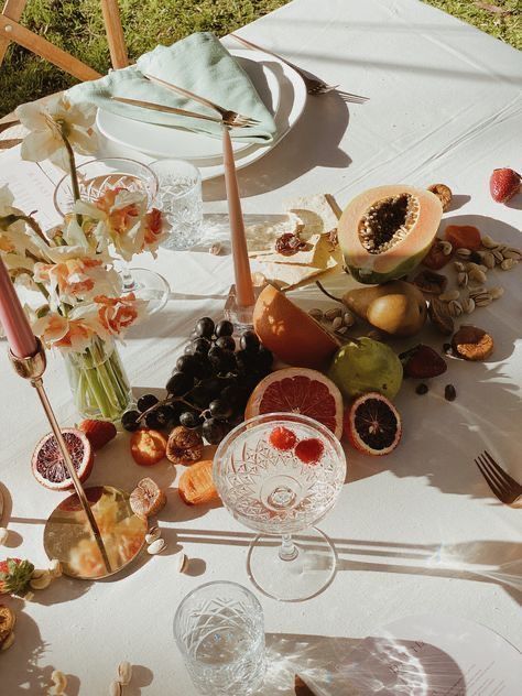 a table topped with plates and glasses filled with food next to fruit on top of a white table cloth