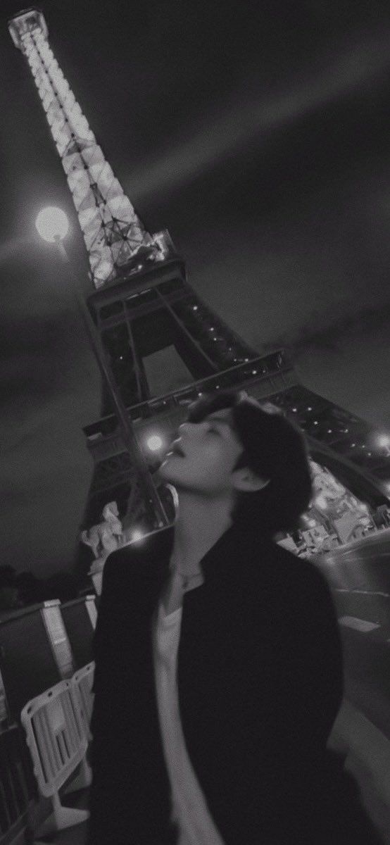 black and white photograph of woman in front of the eiffel tower at night