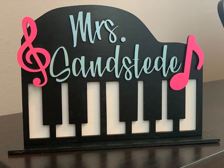 a wooden sign that says mrs and the piano keys are pink, black and white