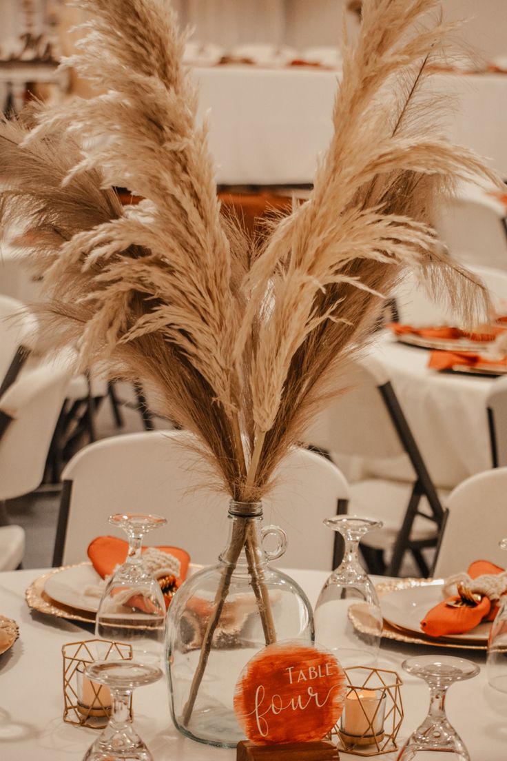 the table is set with white linens and orange napkins, as well as some dried grass