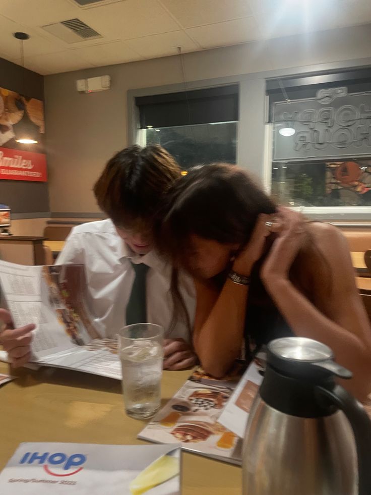 two people sitting at a table with papers in front of them and a coffee pot