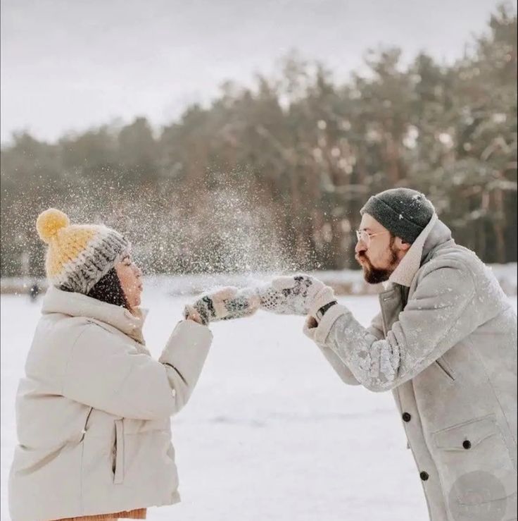 two people standing in the snow, one is throwing snow at the other