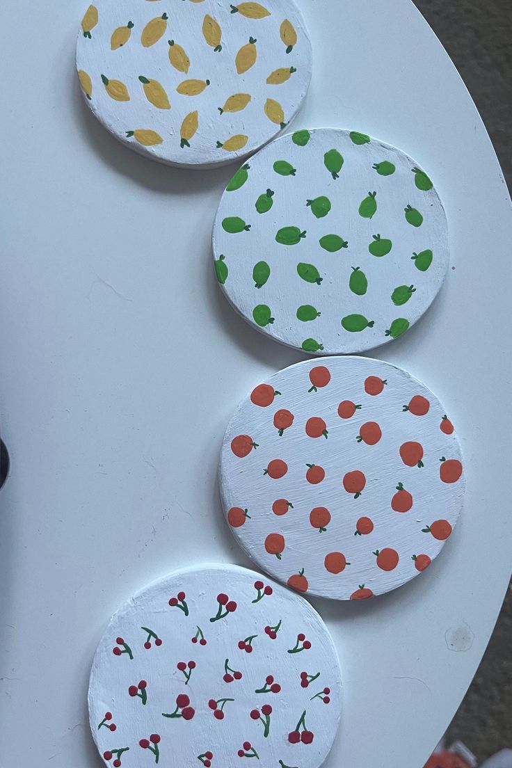 four paper plates with fruit designs on them sitting on a white table next to a black bottle