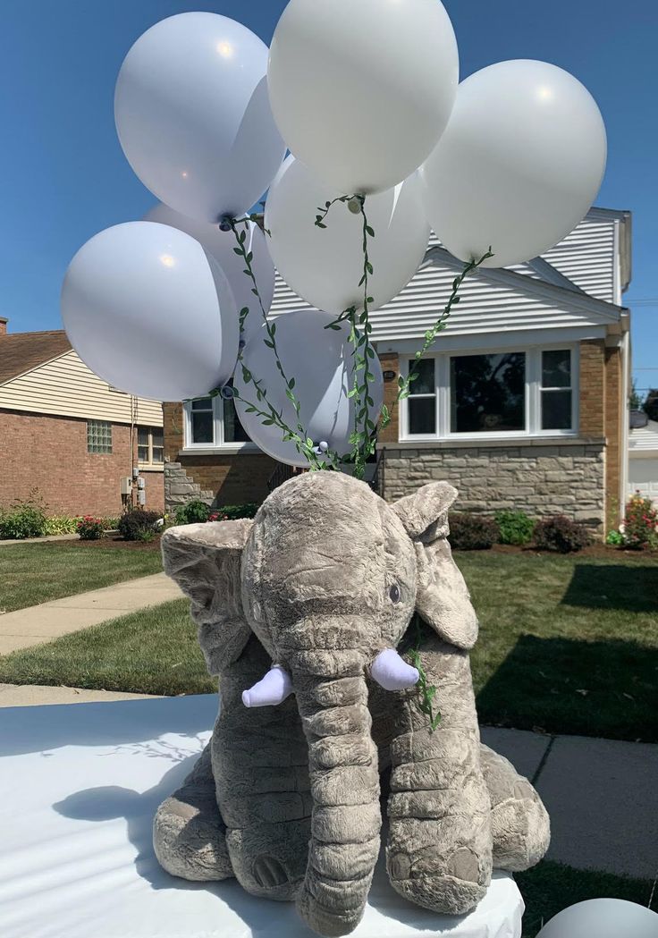 an elephant sitting on top of a table with white balloons attached to it's trunk