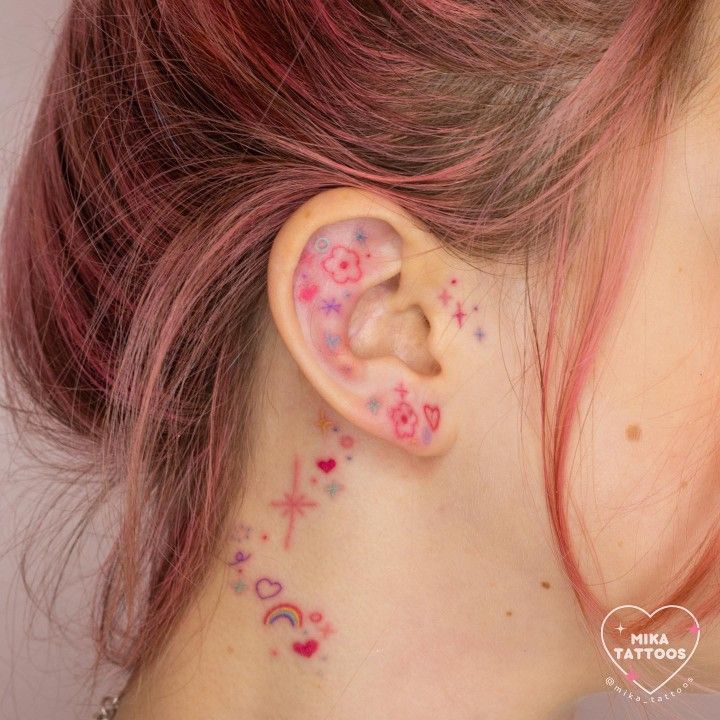 a woman with pink hair has tattoos on her ear and behind the ear is a cross, heart, and star