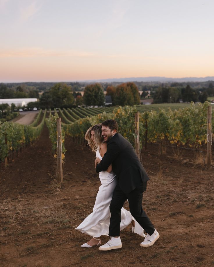 a bride and groom are hugging in the middle of a field with rows of vines