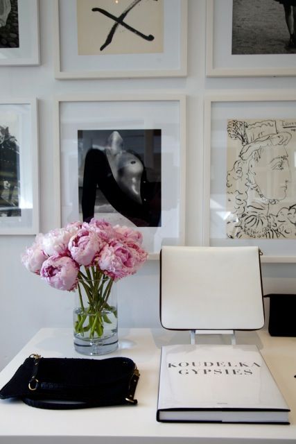 a white desk topped with a vase filled with pink flowers next to pictures on the wall