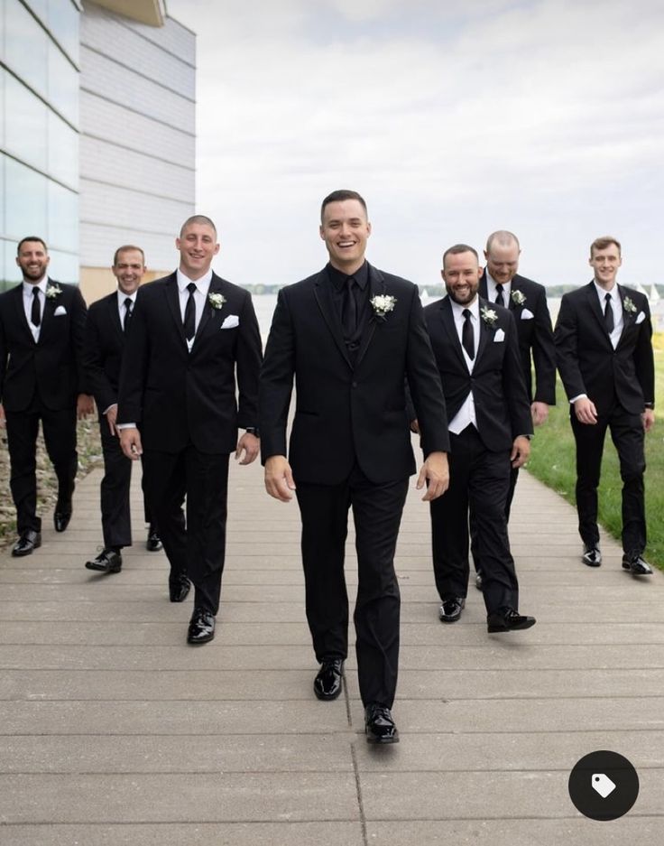 a group of men in tuxedos walking down a sidewalk next to each other