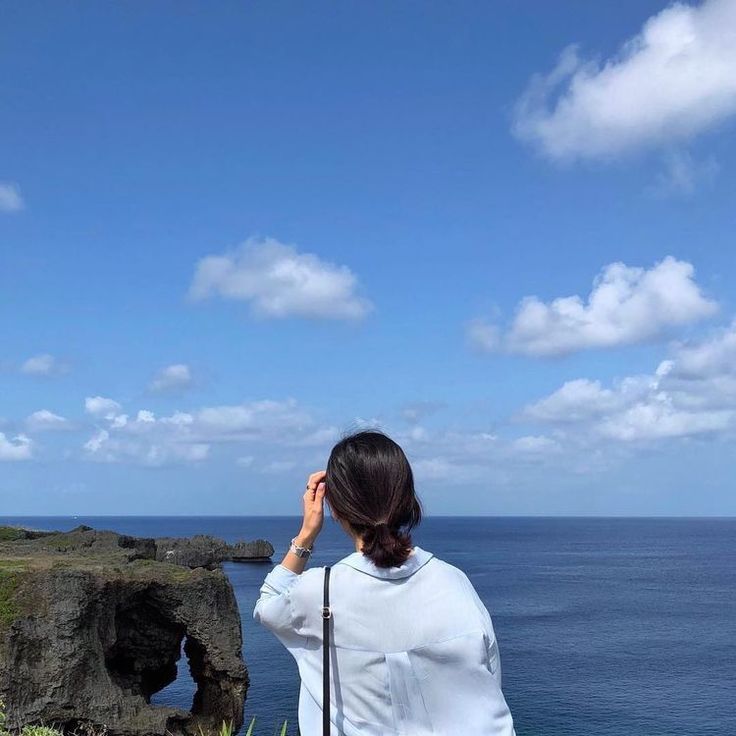 a woman standing on top of a lush green hillside next to the ocean looking into the distance