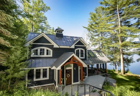 the house is surrounded by pine trees and has a porch with stairs leading up to it