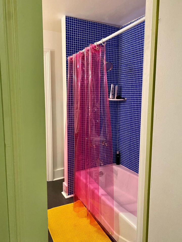 a bathroom with a pink shower curtain next to a bathtub and yellow rug on the floor