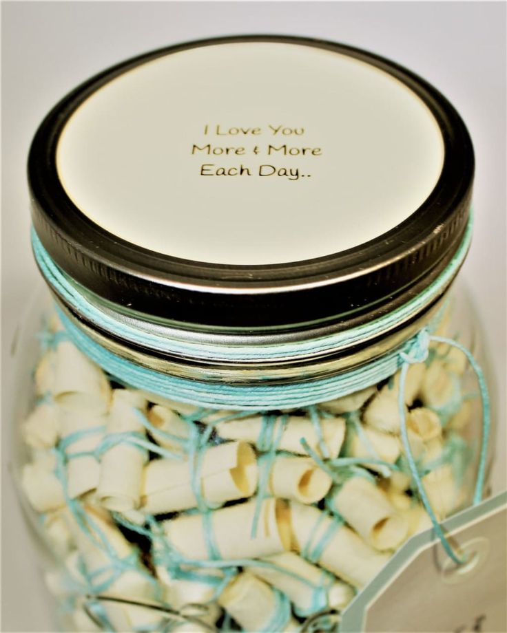 a glass jar filled with white and blue macaroni shells next to a tag that says i love you more than each day