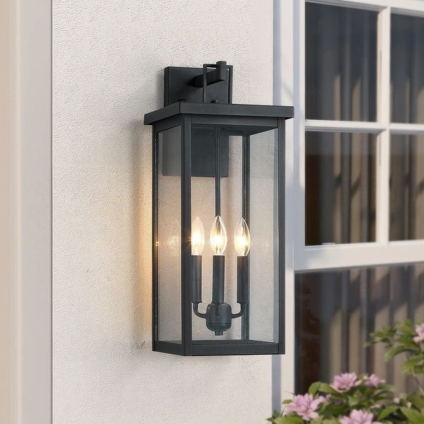 an outdoor wall light with three lights on it and flowers in front of the window