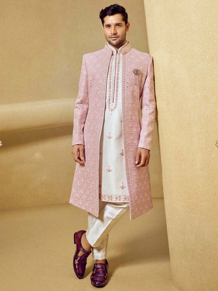 a man standing next to a tall pillar wearing a pink coat and white pants with maroon shoes