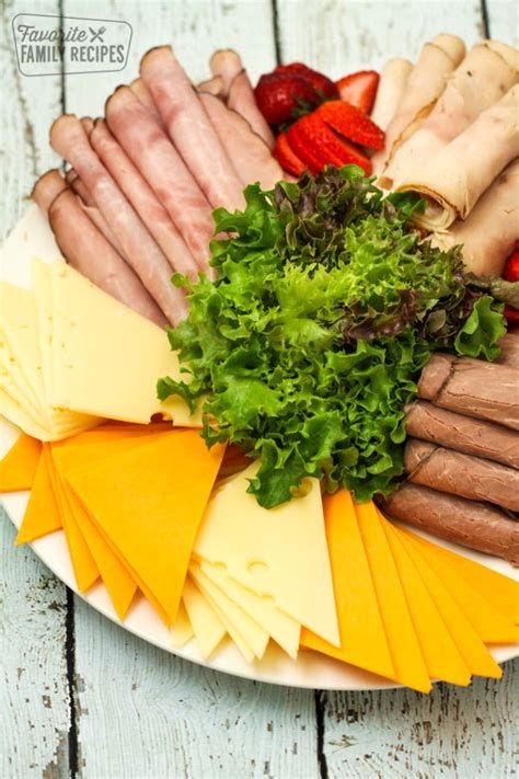 an assortment of cheeses, meats and vegetables on a plate with strawberries