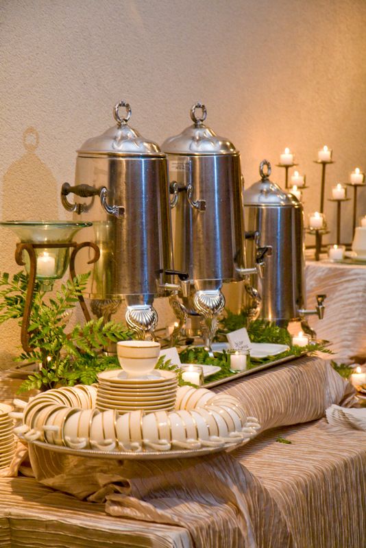 a table topped with lots of silver pots and pans covered in greenery next to candles