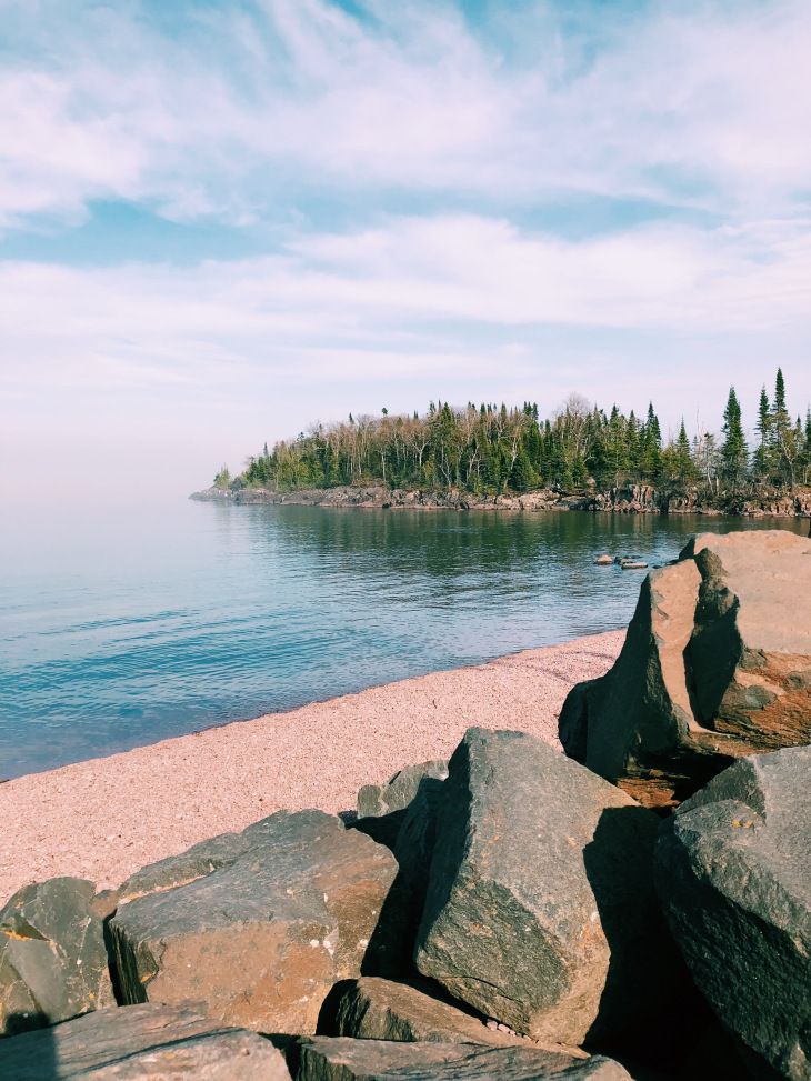 the beach is lined with large rocks and trees in the distance, along with an island