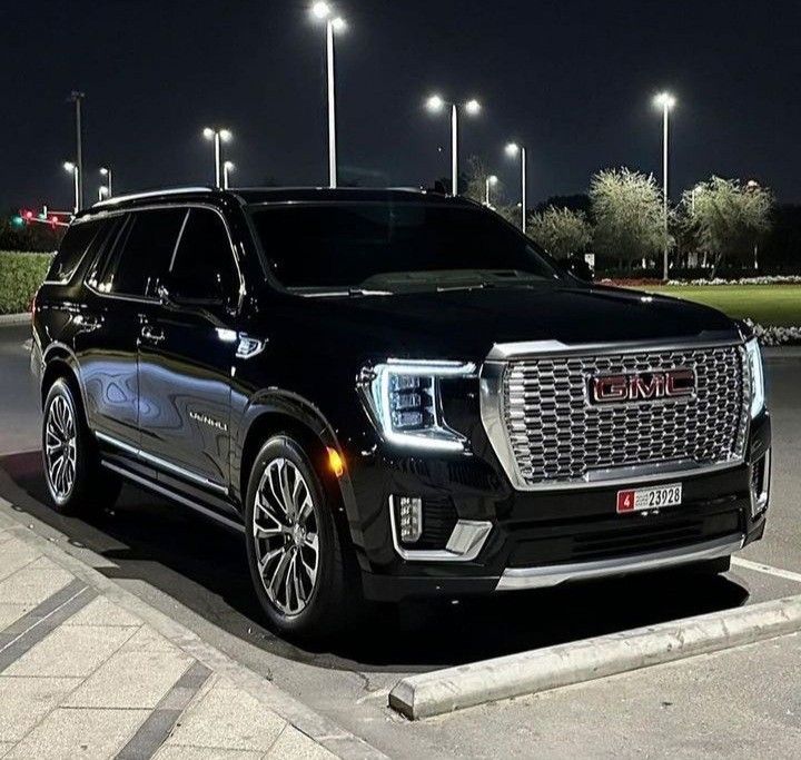 a black suv is parked in a parking lot at night with street lights behind it