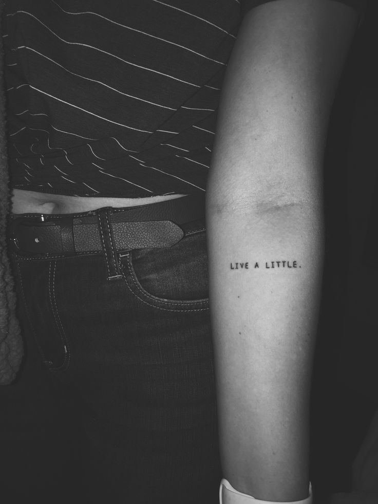 a person with a tattoo on their arm saying live a little