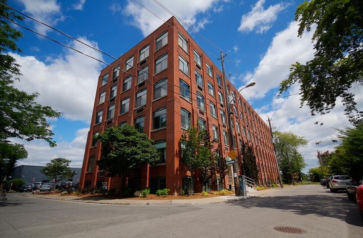 a red brick building with many windows on the corner and cars parked in front of it