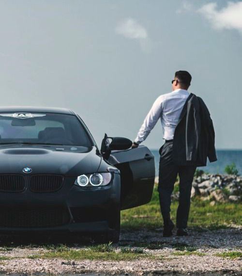 a man standing next to a black car near the ocean