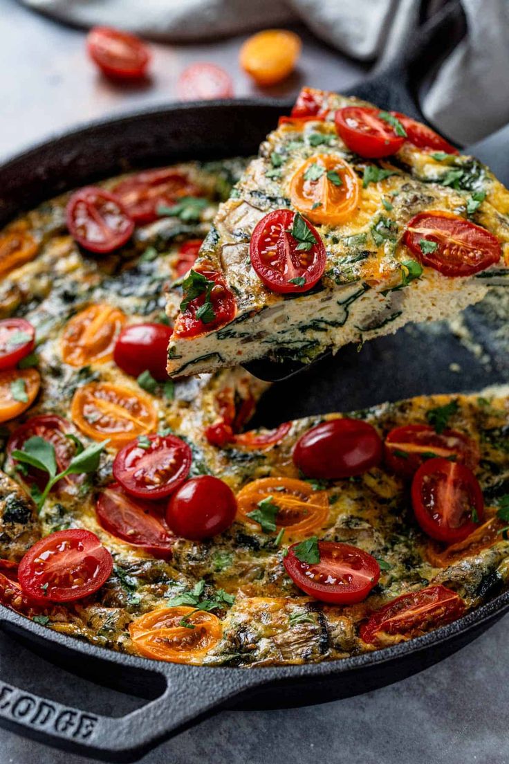 an omelet with tomatoes and spinach is being lifted by a spatula