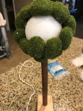 a green wreath on top of a wooden pole with a white ball in it and a cord