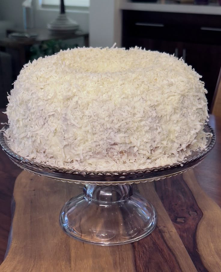 a white cake sitting on top of a wooden table next to a glass plate filled with frosting