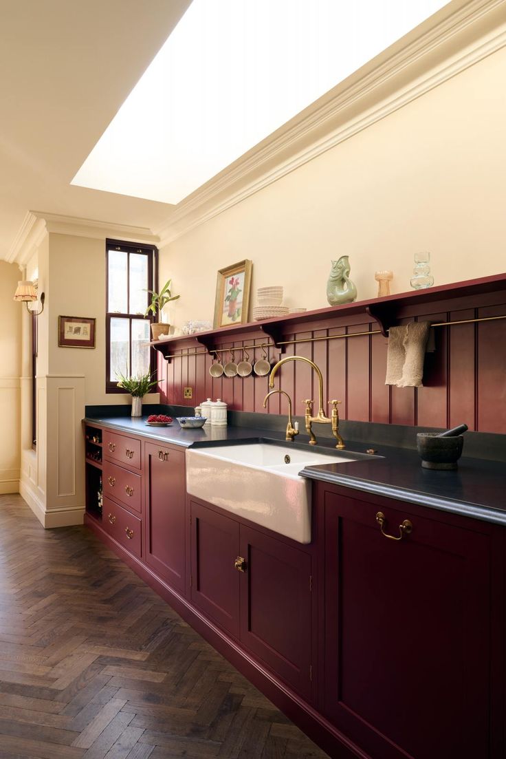 a kitchen with wooden floors and red cabinetry, along with a white sink in the center