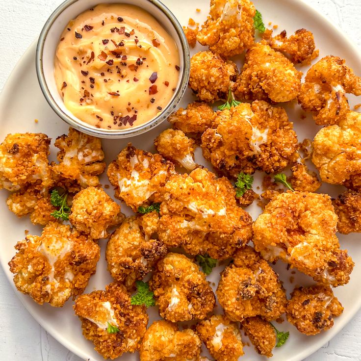 a white plate topped with fried cauliflower next to a dipping sauce