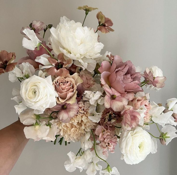 a bouquet of flowers is being held up by someone's hand in front of a white wall