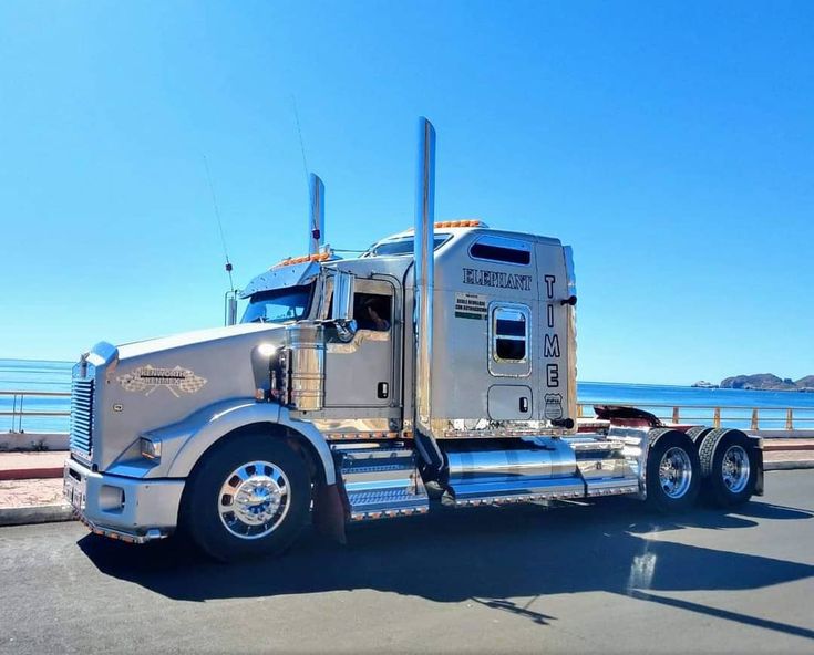 a large semi truck parked on the side of the road near the ocean and mountains