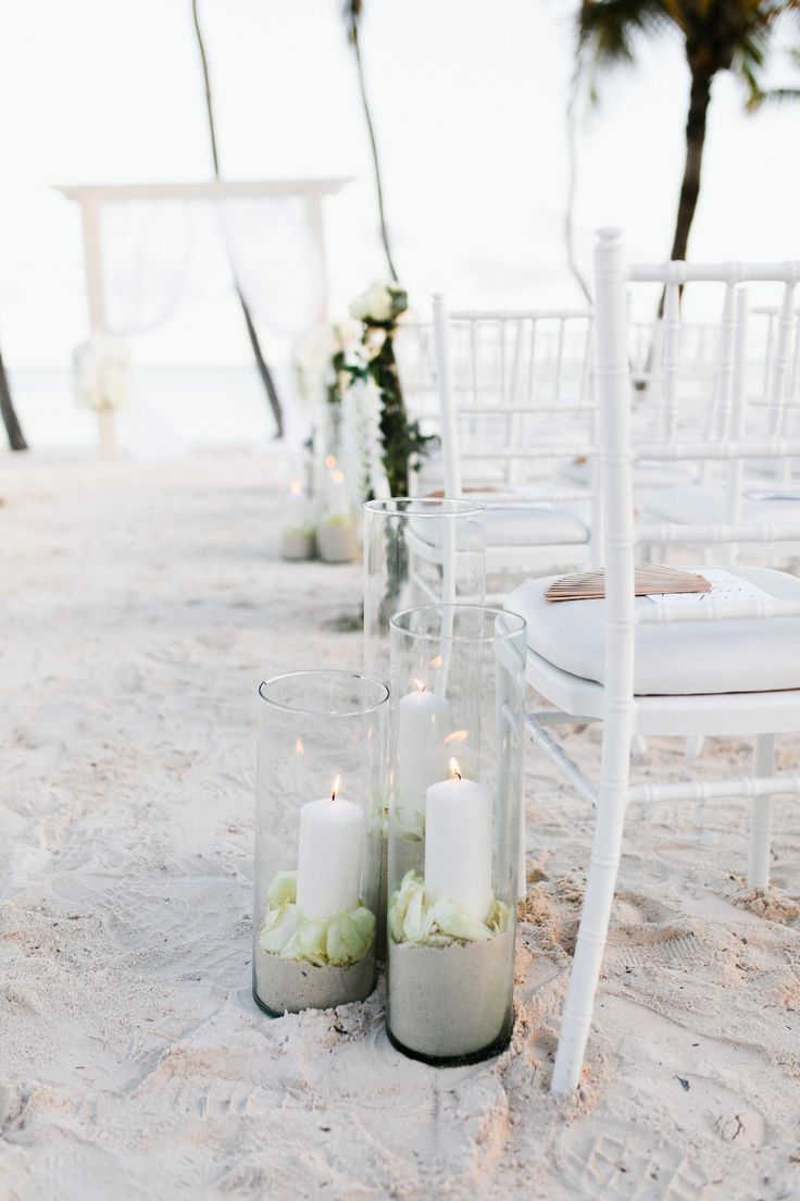 wedding ceremony setup on the beach with white chairs and flowers in glass vases at the end