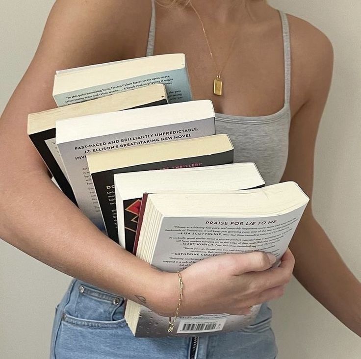 a woman is holding several books in her hands while wearing a tank top and jeans