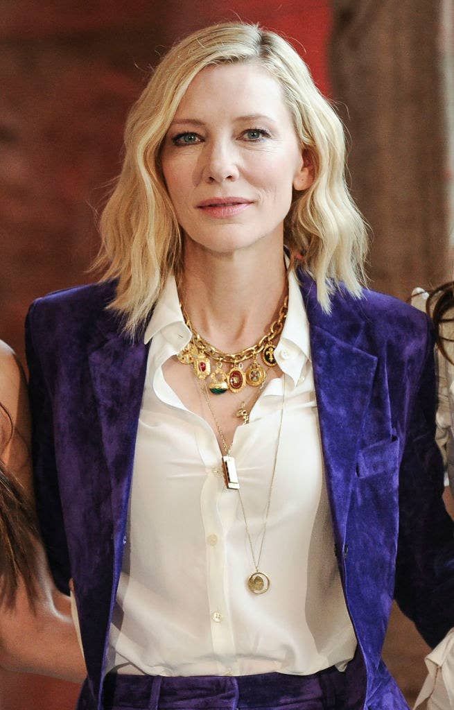 a woman with blonde hair wearing a purple jacket and white shirt is looking at the camera