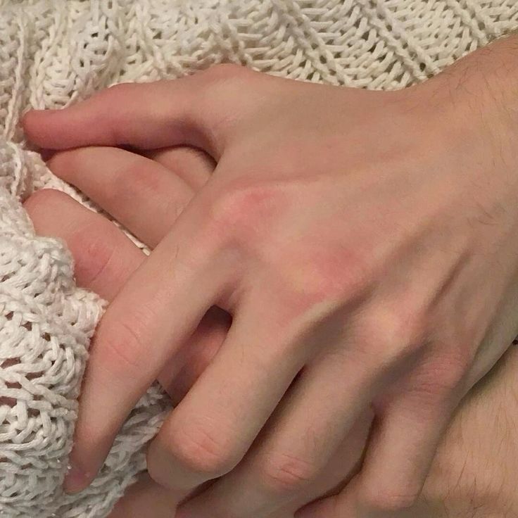 two hands holding each other on top of a white knitted blanket, with one hand touching another