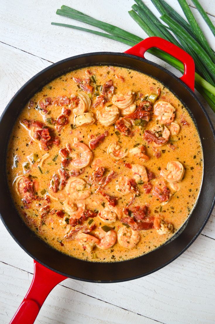 a skillet filled with shrimp and sauce on top of a white wooden table next to green onions