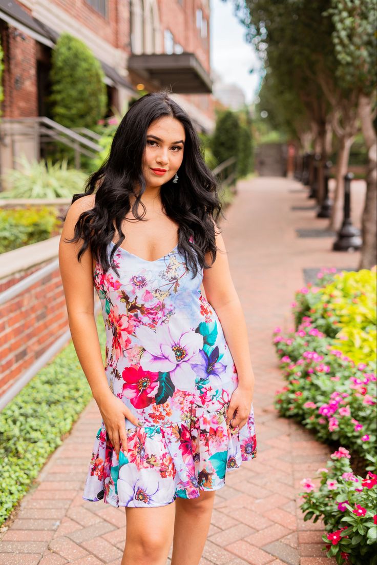 a woman in a floral dress posing for a photo on the sidewalk with flowers around her