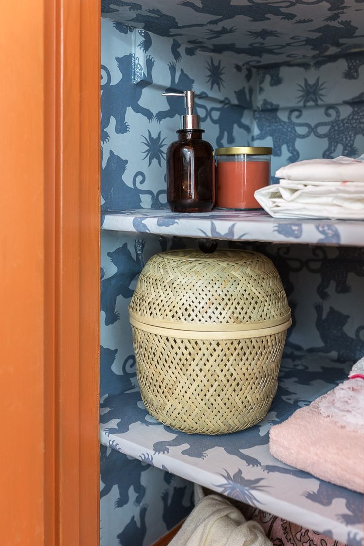 a shelf with towels and other items on it in a room that has blue floral wallpaper