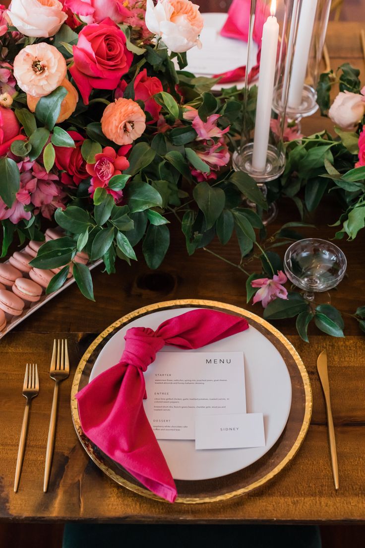 the table is set with pink and orange flowers, silverware, and napkins