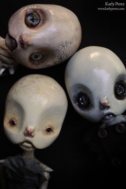 three creepy looking alien dolls with one staring at the camera while another looks up and down