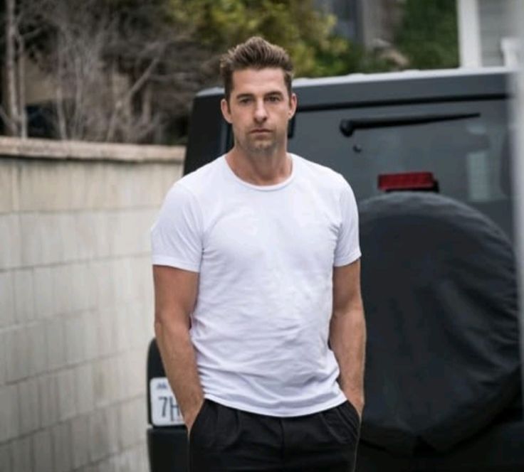 a man in white shirt and black pants standing next to a van with his hands in his pockets