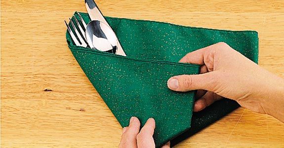 a person holding a green cloth with silverware in it on top of a wooden table