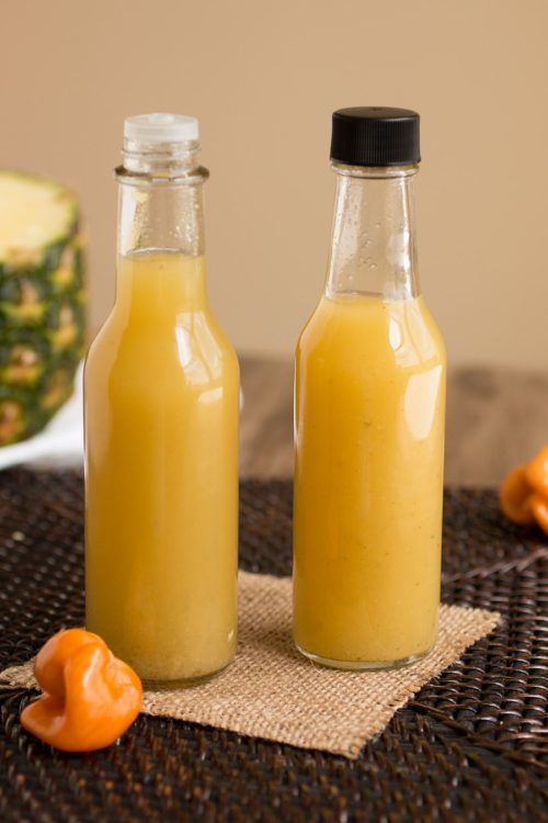 two glass bottles filled with orange juice sitting on top of a table next to some fruit