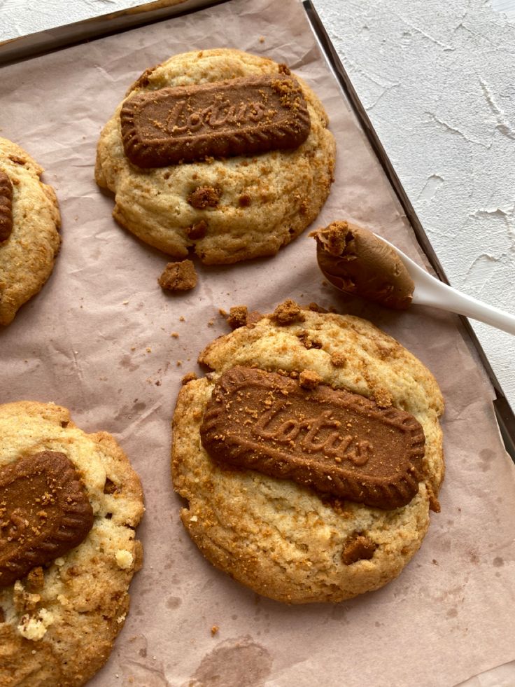 four cookies with chocolate frosting on top sitting on a piece of parchment paper next to a spoon