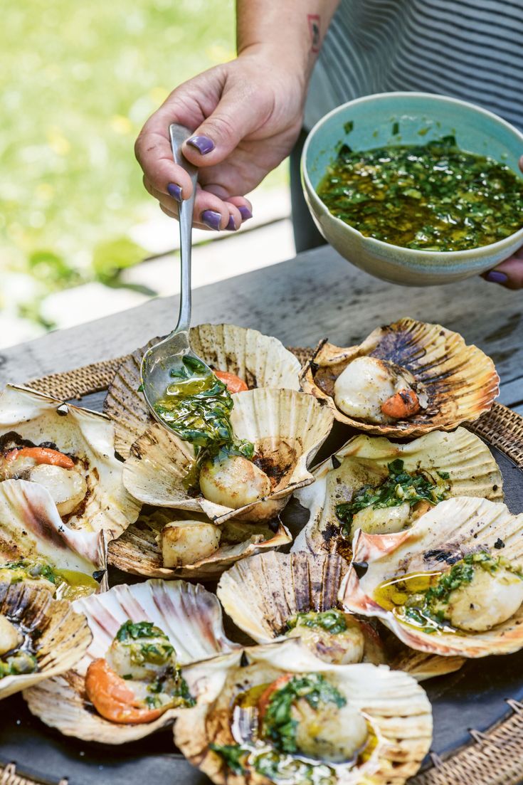 a person holding a spoon over some clams