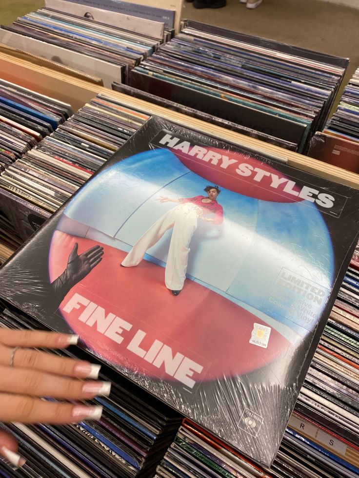 a person holding up a vinyl album in front of a shelf full of cds and records