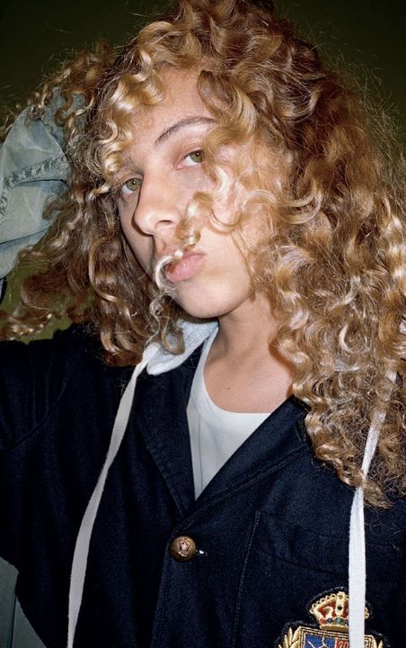 a woman with curly hair wearing a school uniform and looking off to the side while holding her hand on her head