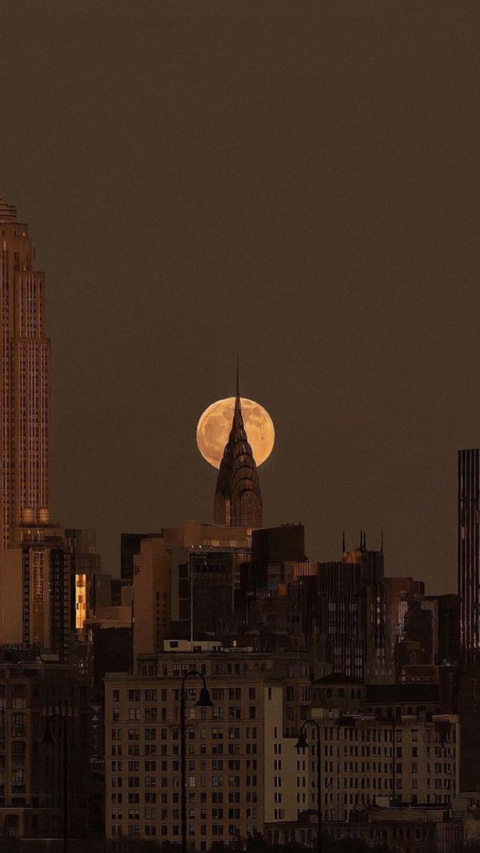 the full moon is seen over a city skyline